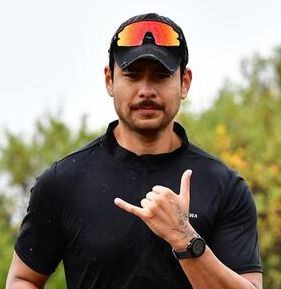 Person in black shirt and cap making a hand gesture outdoors.
